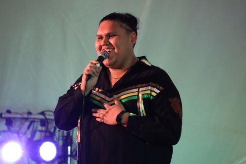 Image shows Mikey "Dizzy Feet" Harris speaking at event. There are purple lights next to him on the left and a white background behind him.