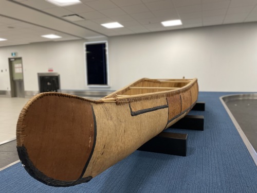 The 19 foot canoe that will be at the airport all summer. It sits on top of a blue carpet at the airport.