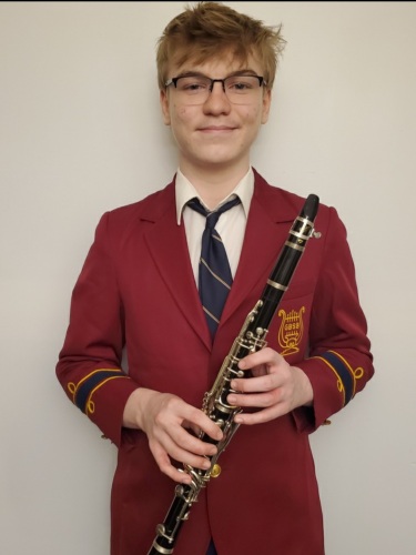 Ethan Walter with his clarinet. He is wearing a red blazer with a gold crest of a harp on it.