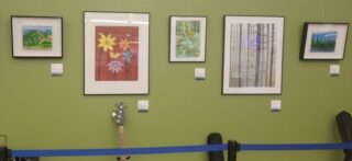 Un petit échantillon des oeuvres exposées sur place, avec des oeuvres colorées de différentes tailles, encadrées sur un mur vert.