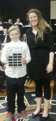 Photo of a young Ethan Walter with his mother. He holds up an award plaque in a gymnasium at a school.