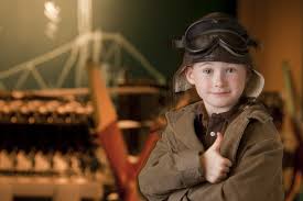Un jeune enfant portant un gilet brun et un chapeau en avant d'une maquette d'avion.