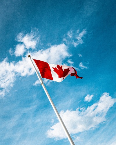 Un drapeau du Canada sur un mât contre un ciel bleu avec des nuages blancs.