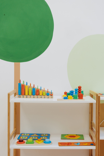 Des étagères avec des jeux pour enfants en avant d'un mur blanc, vert et brun.
