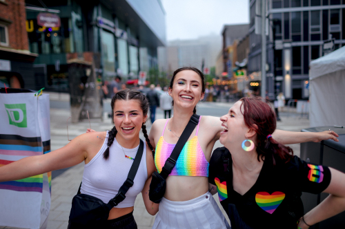 Three women smiling and wearing colourful clothes during the TD pride block party. 