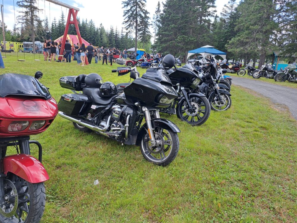 Plusieurs motos de marque populaire devant des festivaliers regroupés ensemble durant un festival de moto lors d'une journée chaude et nuageuse