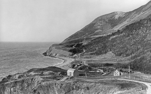 Une ancienne photo démontrant une maison et une grange au pieds des montagnes.