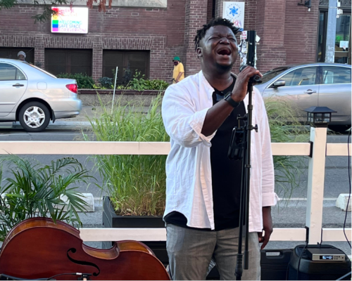 A person in a white shirt is singing outside on the street. 