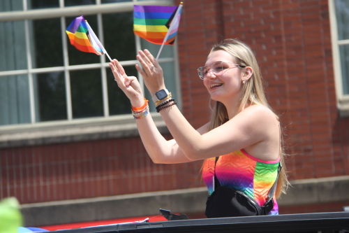 Photo of a woman with two pride flags hanging out of a car.