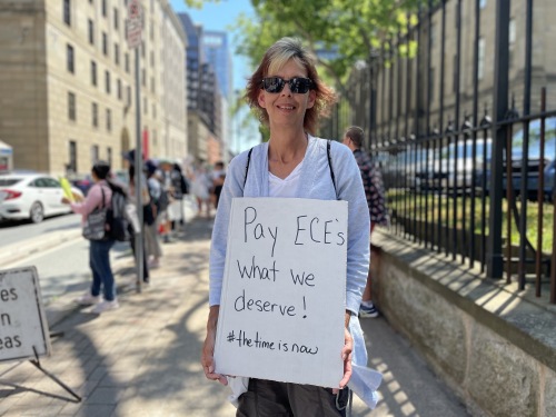 A woman stands outside holding a sign that says "Pay ECE's what we deserve" at the protest on Tuesday.