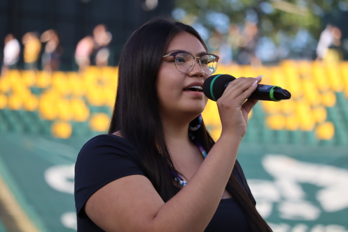An Indigenous woman stands and sings into a microphone at Commonwealth Stadium.