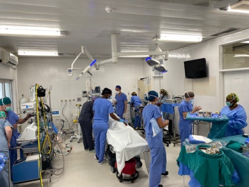 Photo of an operating room with doctors in scrubs and equipment and beds.