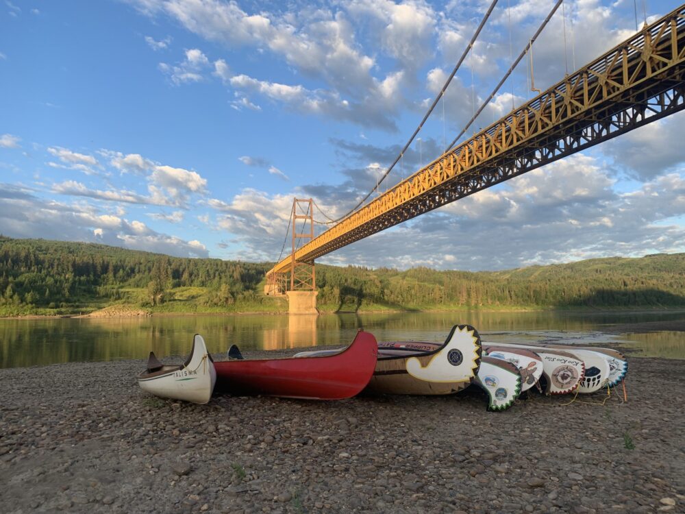 8 canoë sont placés sur le banc de la rivière. En arrière, le pont jaune de Dunvegan.