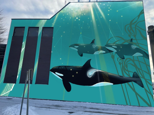 Painting of three orcas swimming on a blue background on the side of a building that has three vents