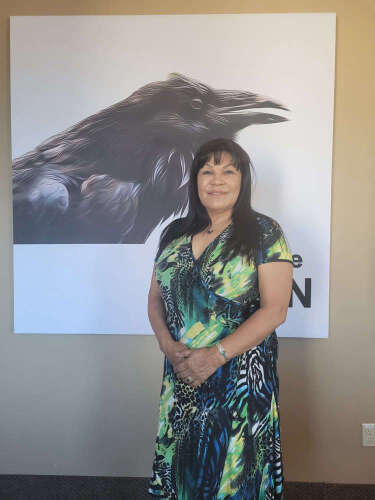 Marlene Poitrais stands against a black and white poster featuring a raven.