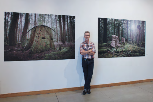 David Ellingsen stands in between two large prints of his photographs depicting tree stumps.