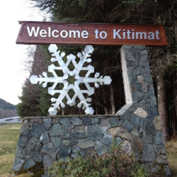 A wooden sign reading Welcome to Kitimat with a large metal snowflake perched on a stone base underneath