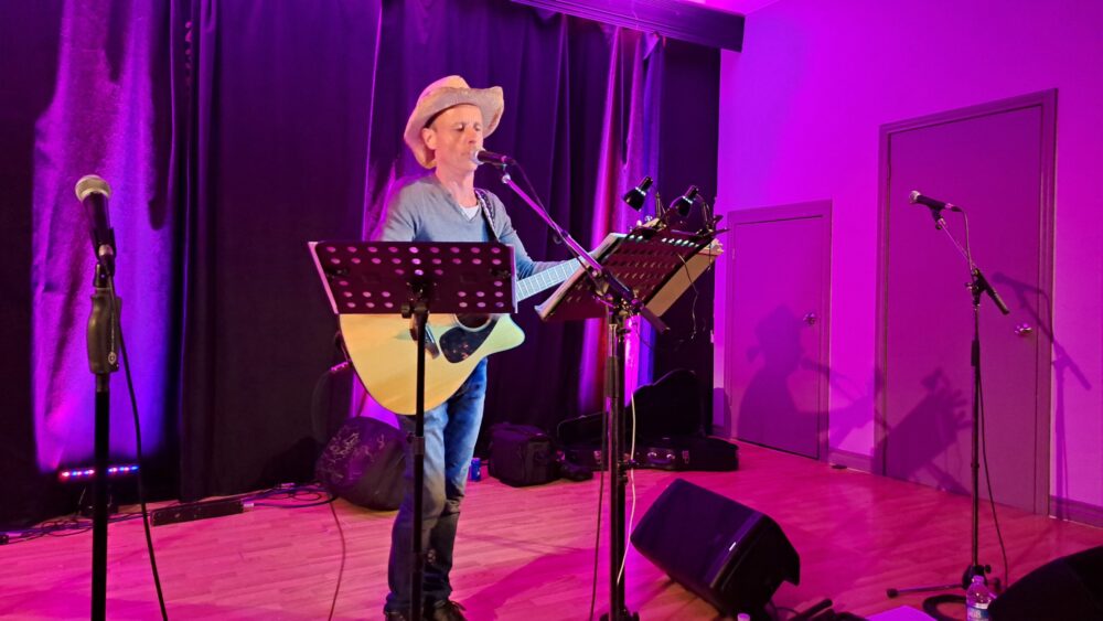 Un chanteur tenant sa guitare et portant un chapeau de cowboy, en performance durant un concert.