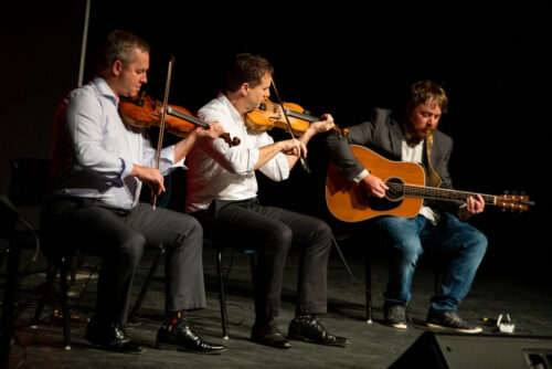 Trois hommes musiciens assis sur des chaises.