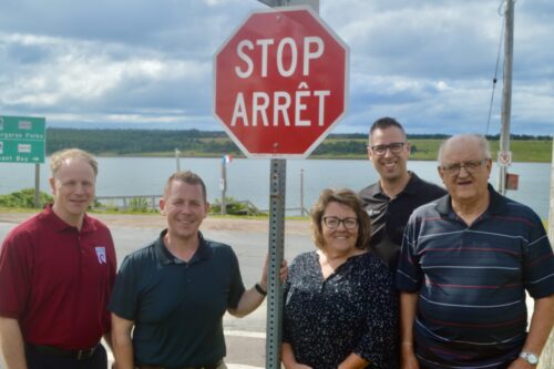 Cinq personnes près d'un panneau d'arrêt bilingue.