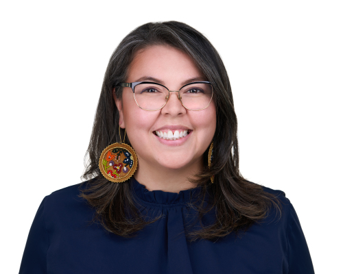 A head shot of an Indigenous woman wearing navy. She stands against a black background.