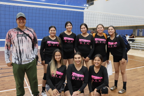 A senior girls volleyball team and head coach pose for a group photo in front of a volleyball net.