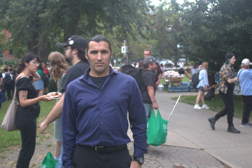 A man wearing a blue shirt stands in front of people walking at a rally.