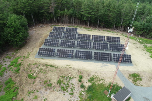 An array of solar panels viewed from above. The panels are surrounded by forest.