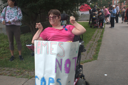 A human rights activist at the rally wearing a pink shirt and using a wheelchair. She carried a white poster that reads "Homes Not Cops"