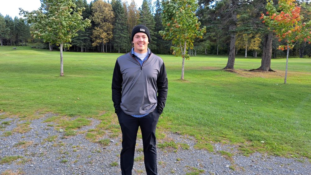 Homme habillé en noir gris debout devant un terrain de golf