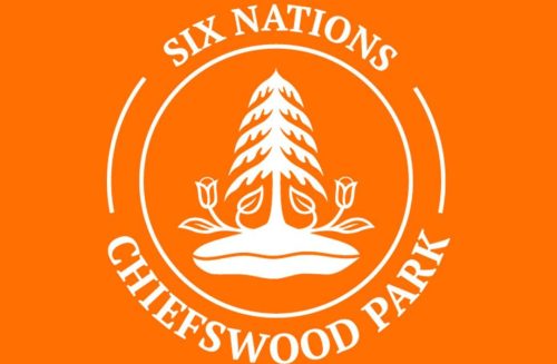 Orange background white text in a circle saying "Six Nations, Chiefswood Park " inside the circle is a white drawing of an evergreen tree