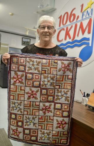 Une dame tenant un tapis en avant du logo de Radio CKJM.