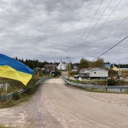 Un drapeau ukrainien flotte au vent. À l'arrière-plan, une église entourée de maisons.