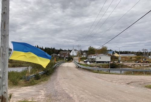 Un drapeau ukrainien flotte au vent. À l'arrière-plan, une église entourée de maisons.