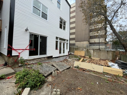 Photo of a wrecked backyard, there is wood on the ground, red tape on the wall and renovations taking place on a white house.