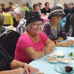 Des femmes avec des chapeaux assises à table en train de prendre le thé.