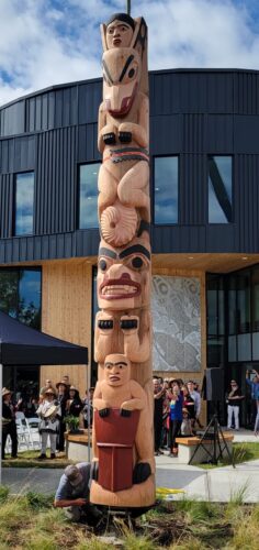 A wood totem pole with the figures of a bear, a wolf, a man and a matriarch at the top
