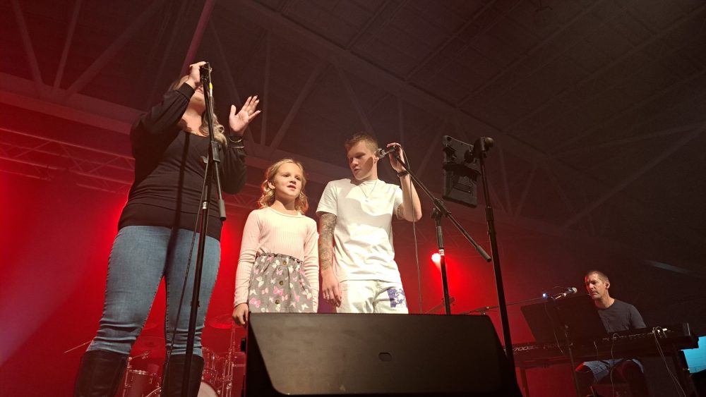 Un femme, une jeune fille et Olivier Bergeron sont sur scène pour chanter une chanson