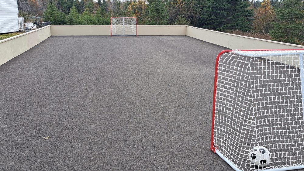 Une patinoire extérieur asphaltée comportant un ballon de soccer et deux filets de hockey