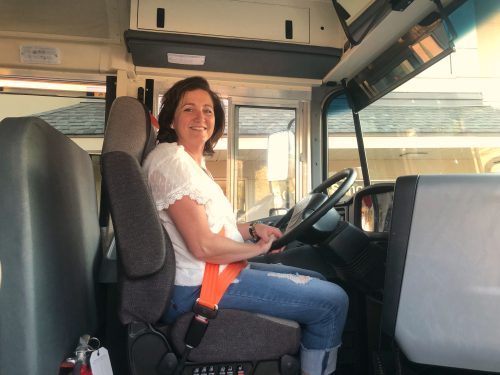 Woman sitting in drivers seat of a bus.