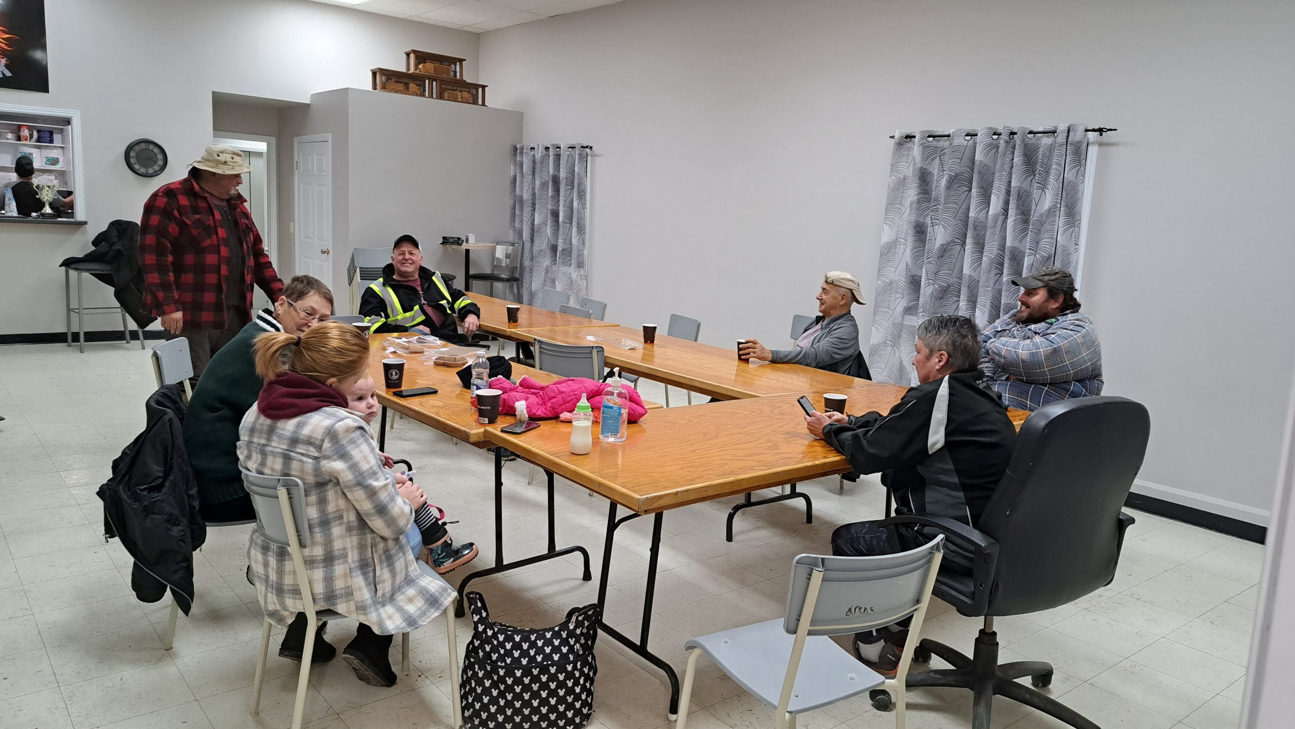 sept personnes sont réunis autour d'une grande table, se réchauffement avec un café à la main dans une salle blanche à l'intérieur d'une caserne de pompier