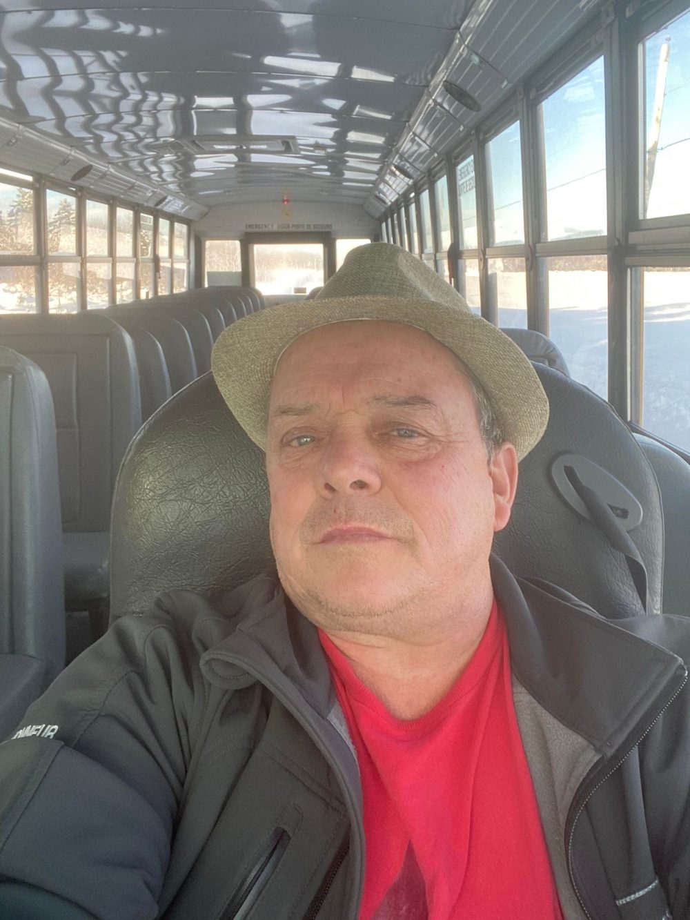 Chauffeur d'autobus au volant de celui-ci. Il porte un chapeau, une chemise rouge et une veste noire