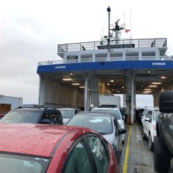 Cars sit on the deck of a ferry boat showing the bridge of the vessel.