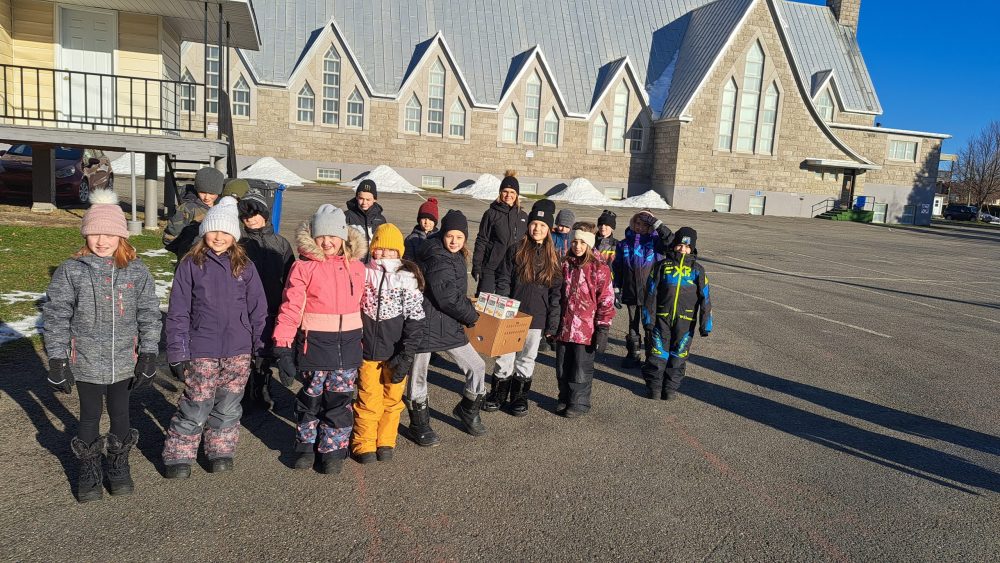 une classe de quatrième année accompagné de leur enseignante, tous habillés manteau d'hiver, à l'extérieur lors d'une journée ensoleillée.