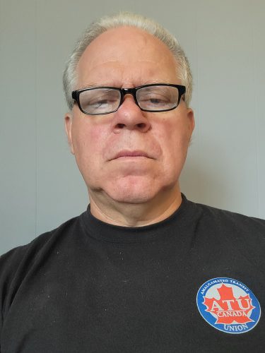 A self-taken photo of a man wearing a black t-shirt and glasses. He stands against a white background.