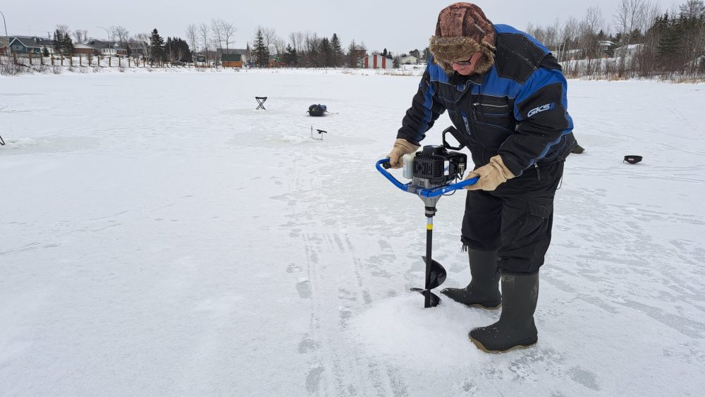 Homme creusant un trou sur un lac gelé afin de pratiquer la pêche sur la glace