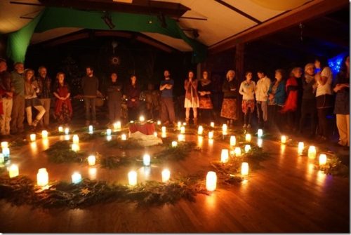 People calmly stand around a large installation of cedar bows and lit candles.