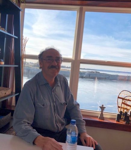 Gary Theriault, un homme dans sa soixante-dixaine, est assis à un bureau devant une fenêtre qui donne sur le quai de l'Anse-des-Belliveau..