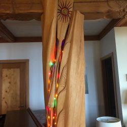 A wooden post carved by an artist shows wavy lines, a paddle and colored lights.