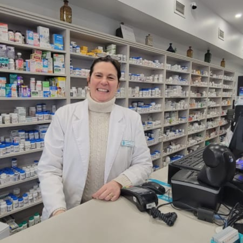 Una mujer sonriendo en un mostrador, detrás de ella una anaquel de medicinas 